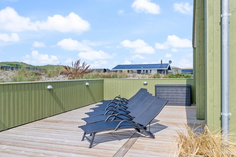 Una terraza exterior con tumbonas reclinables junto a una pantalla verde.