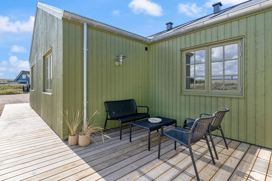 Una terraza junto a una pared exterior verde tiene asientos al aire libre y ventanas.