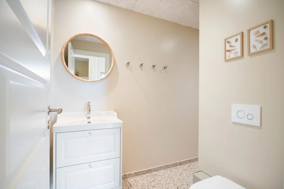 Un baño luminoso con un lavabo blanco y un espejo redondo.