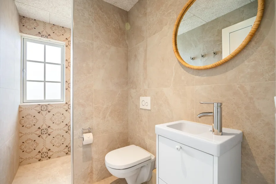 Un baño con lavabo, inodoro y espejo redondo.
