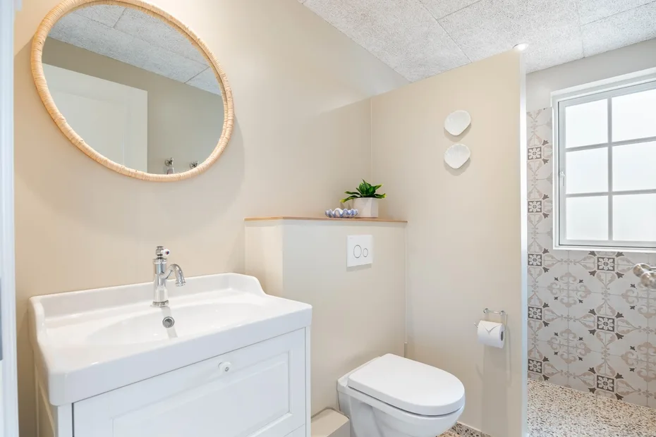 Un baño luminoso con lavabo, inodoro y zona de ducha con azulejos.