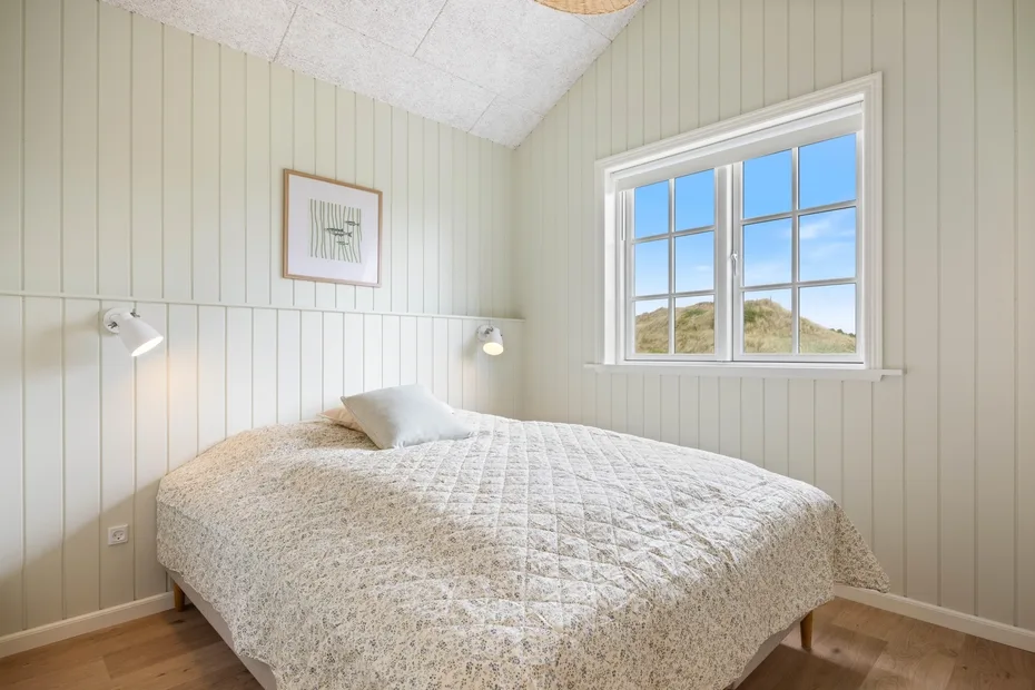 Un dormitorio luminoso con una cama bajo una ventana grande.