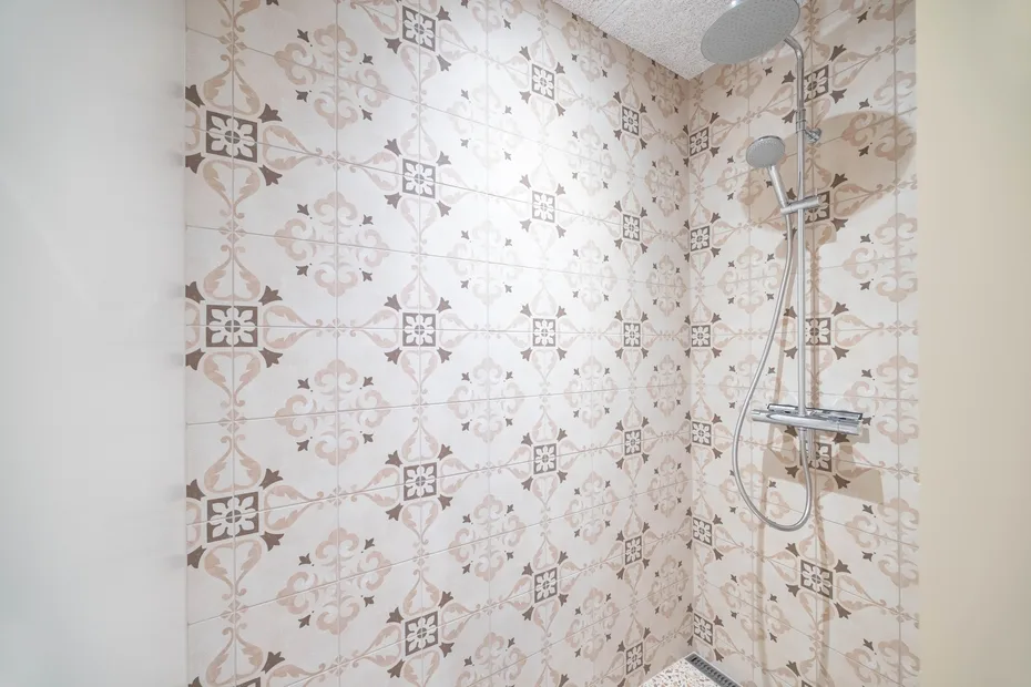 Zona de ducha con paredes de azulejos estampados y una ducha de mano.