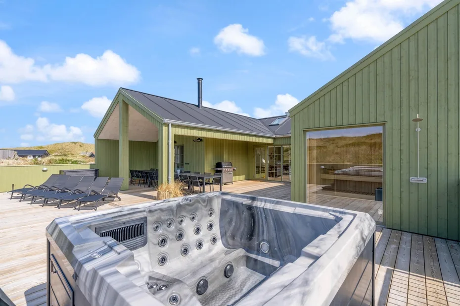 Una bañera de hidromasaje al aire libre está en una terraza junto a una casa verde.