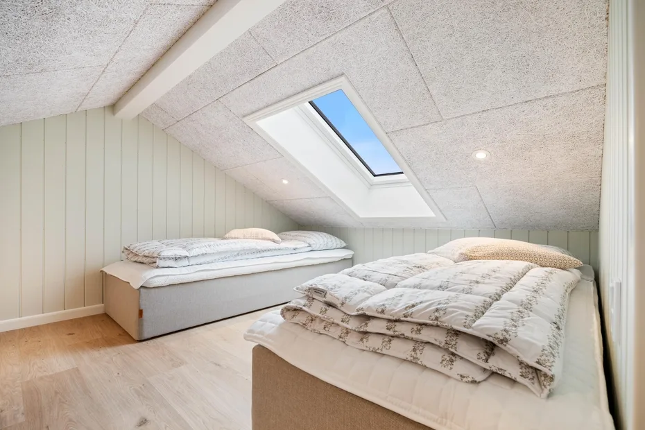 Un dormitorio con techo inclinado, dos camas y una claraboya.