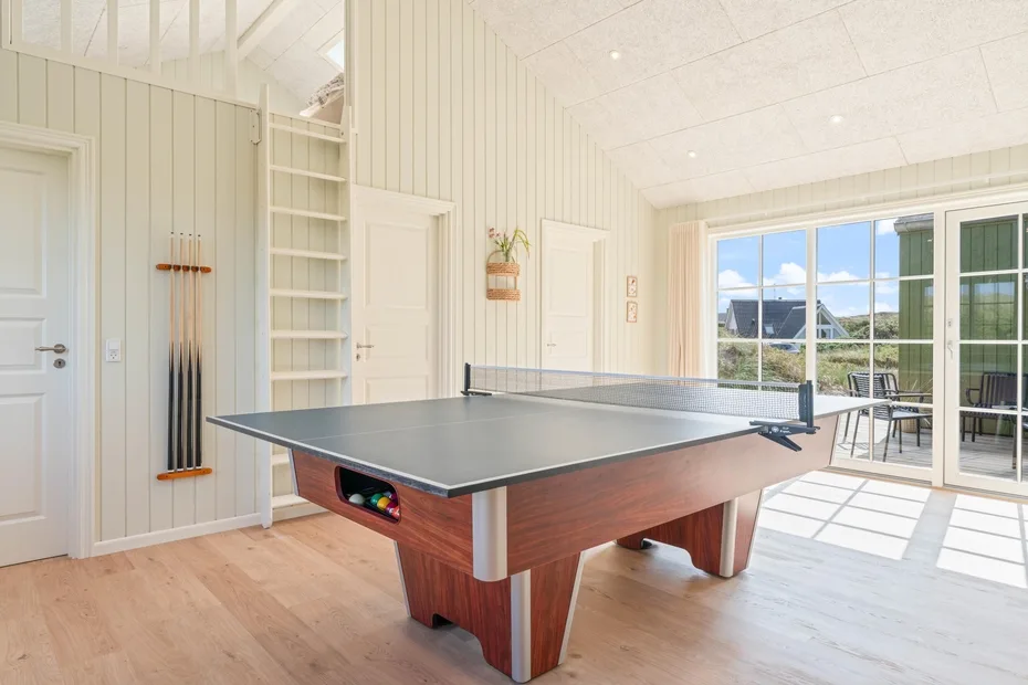 Una luminosa sala de juegos con una mesa de ping-pong y grandes ventanas.