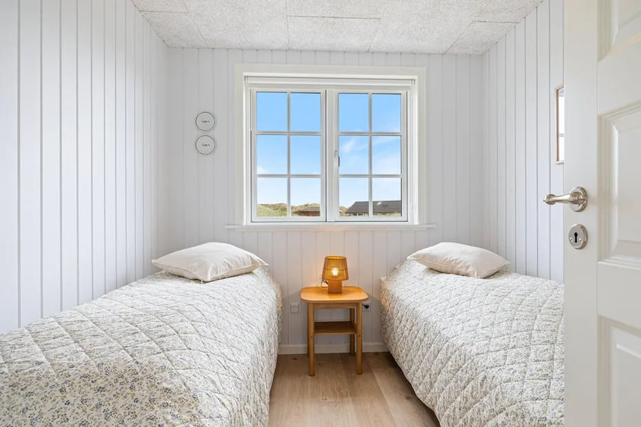 Un dormitorio luminoso con dos camas y una mesita bajo la ventana.