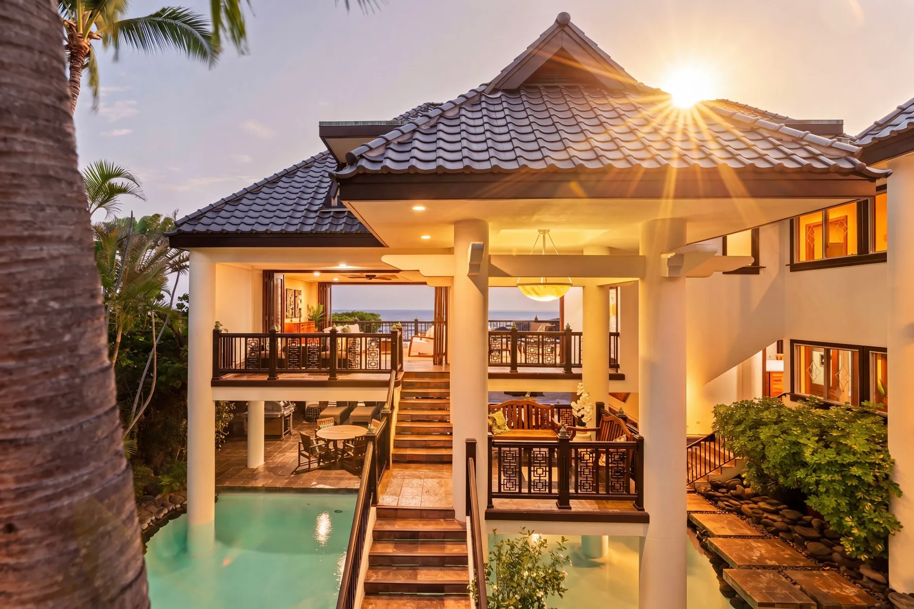 Un edificio de estilo tropical con balcones da a una piscina al atardecer.