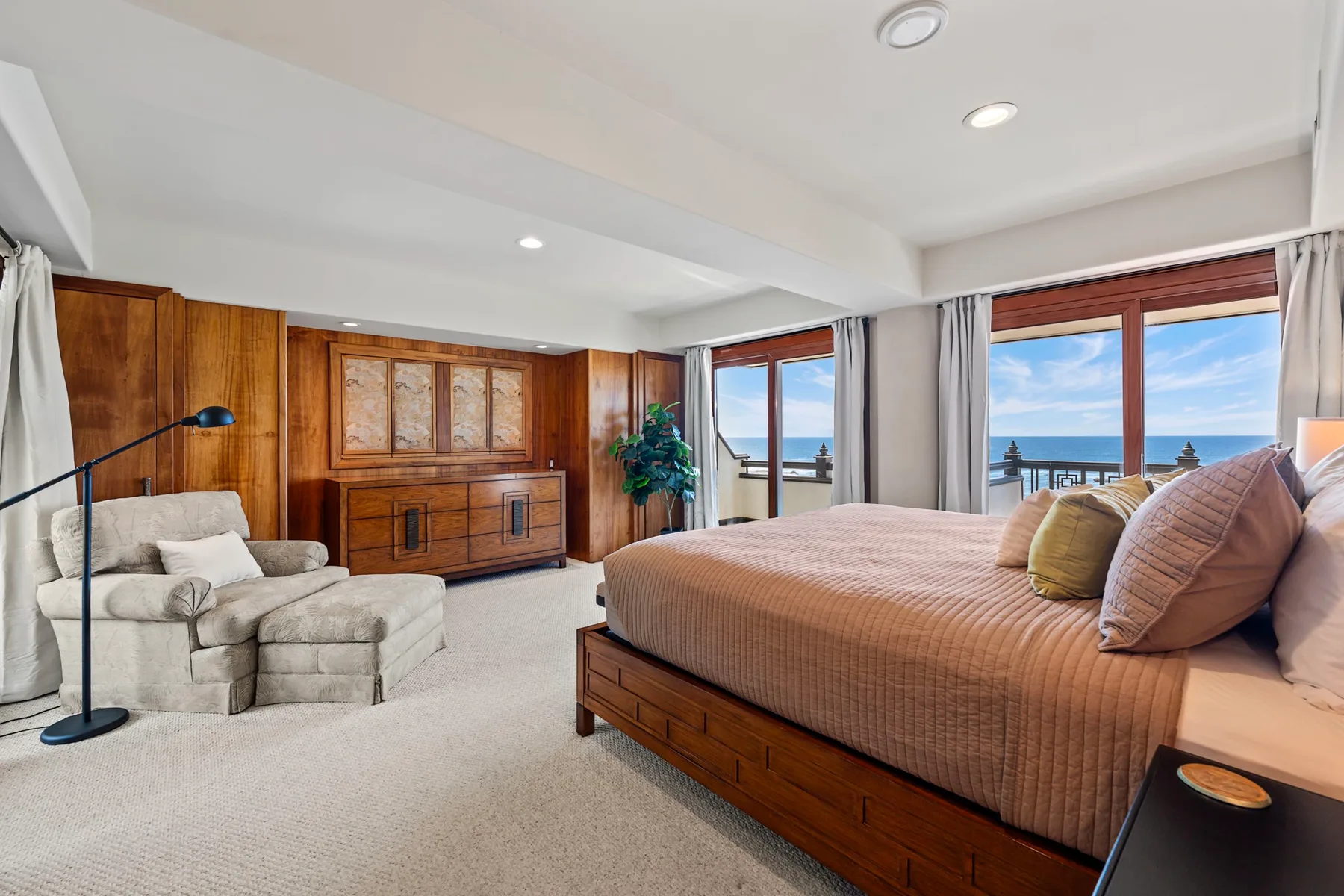 Un dormitorio con una cama grande, paredes revestidas de madera y vistas al mar por las ventanas.