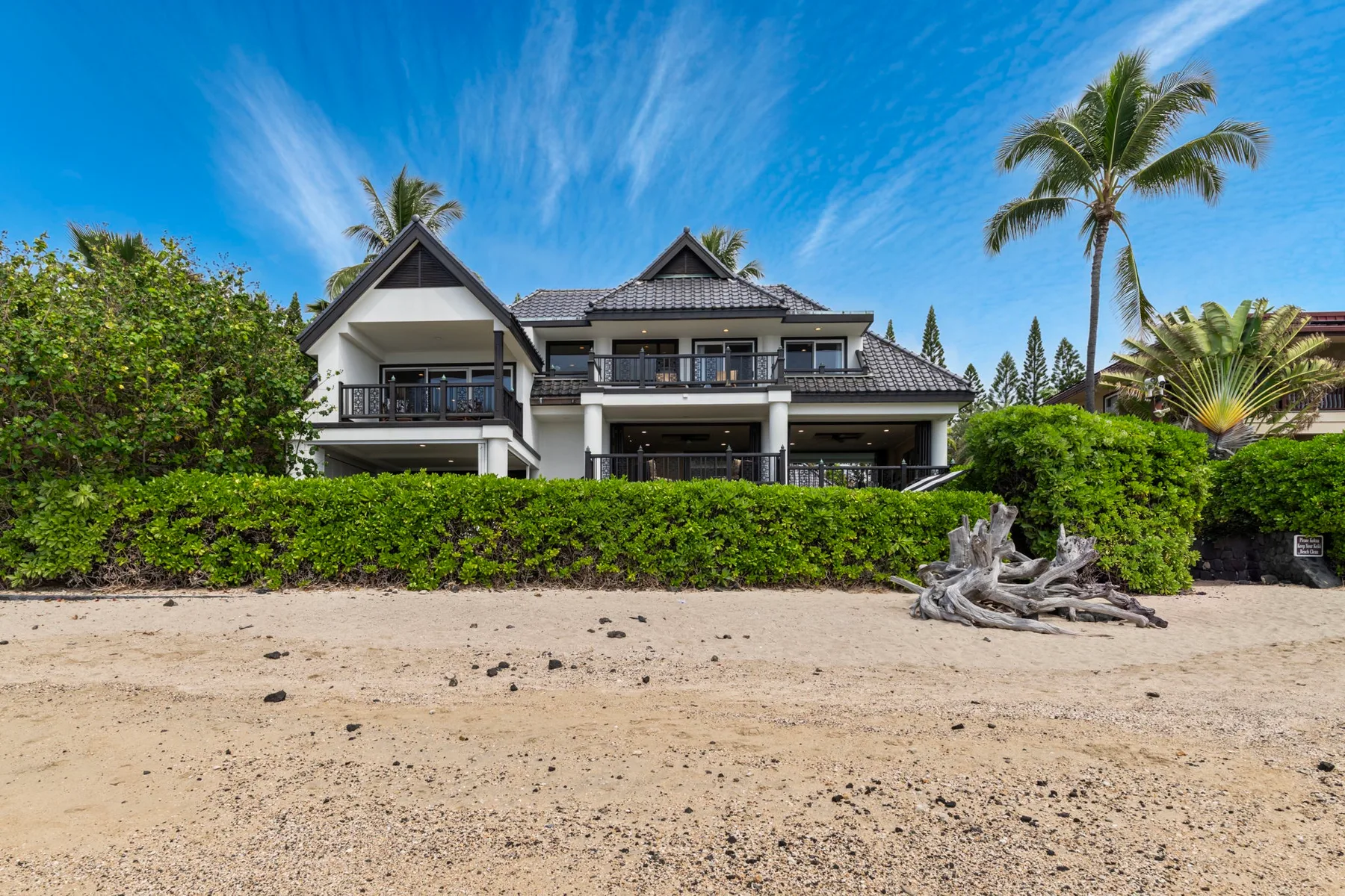 Una casa grande se alza detrás de un seto junto a una playa de arena.