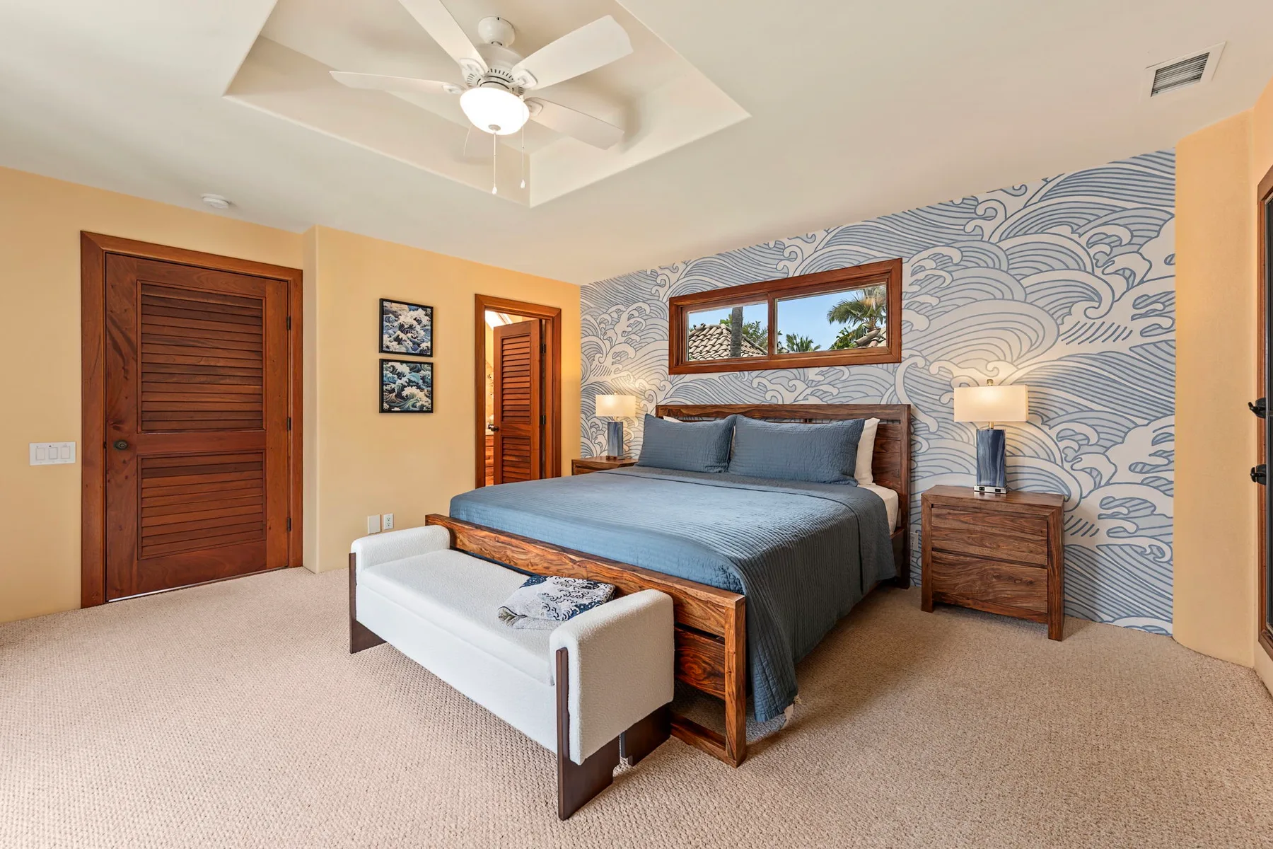 Un dormitorio con una cama frente a una pared azul con motivos de olas y un banco a los pies.