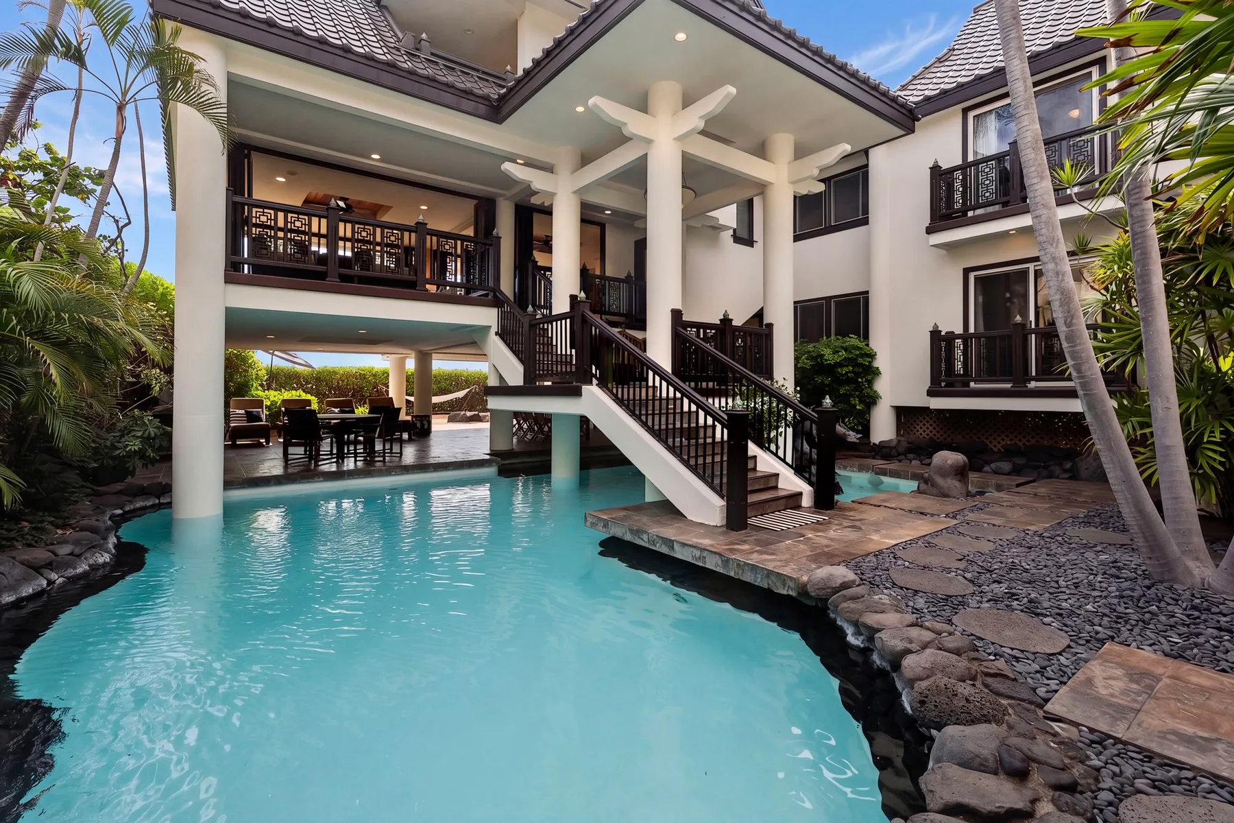 Una piscina junto a una casa de varios pisos, con una escalera que lleva a un balcón.