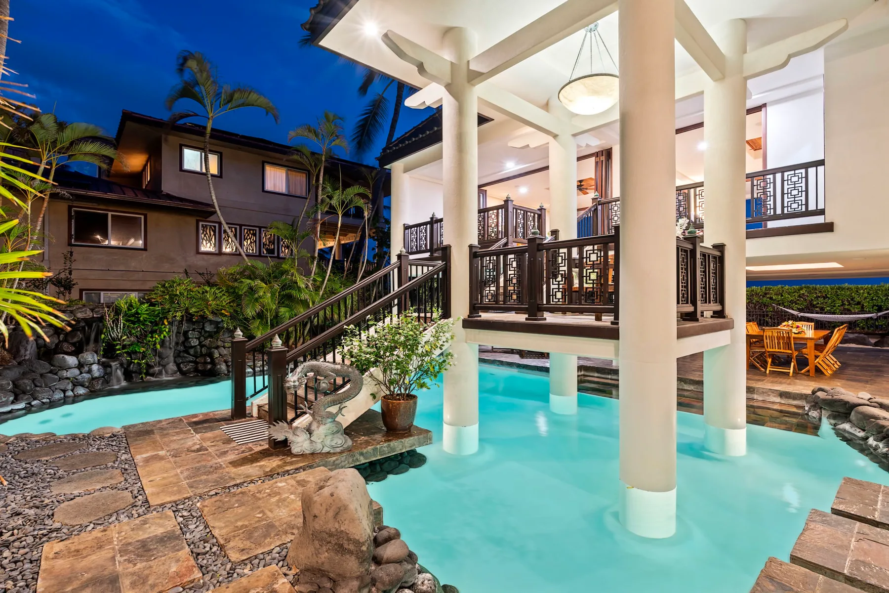 Una piscina de estilo resort rodea un pabellón cubierto con barandillas oscuras.