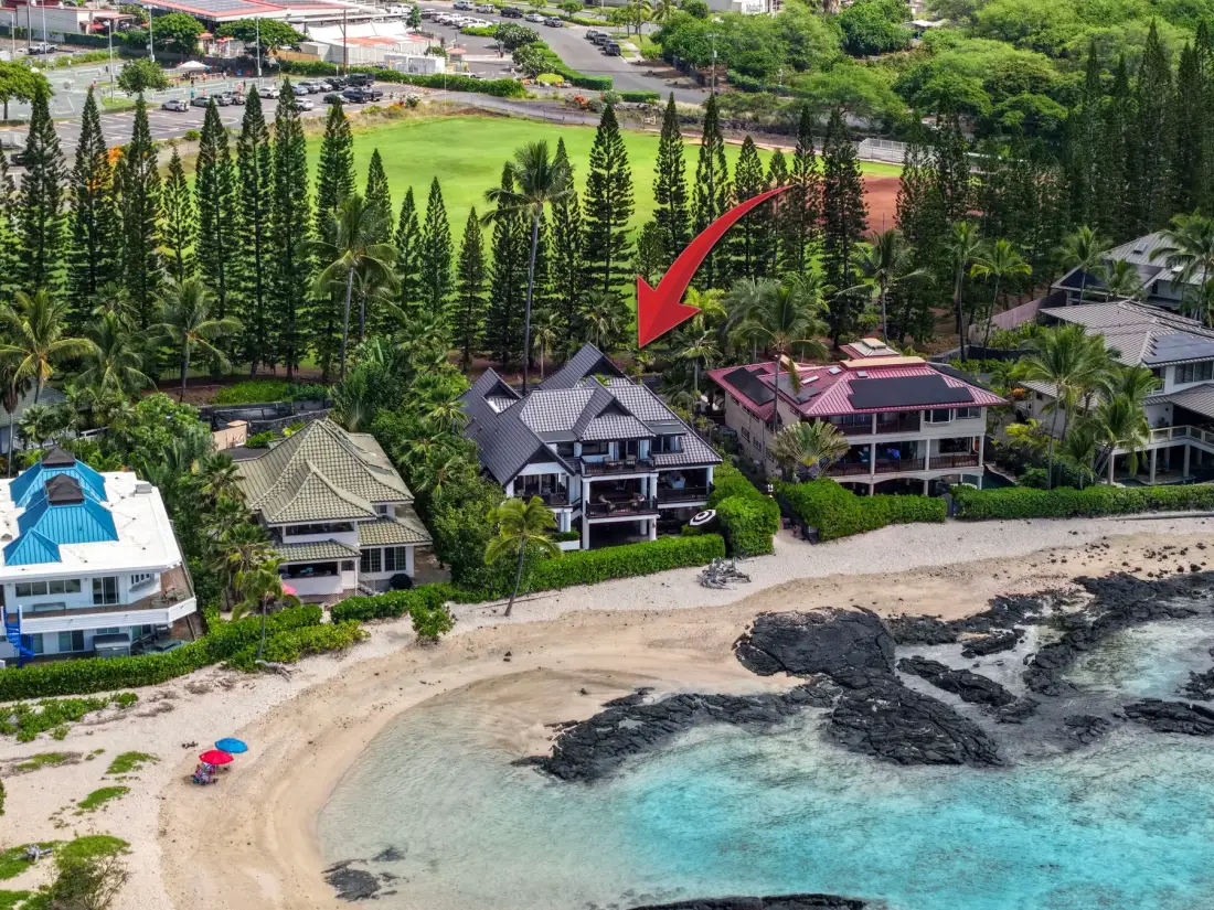 Vista aérea de casas junto a la playa, entre árboles, con arena y agua turquesa.