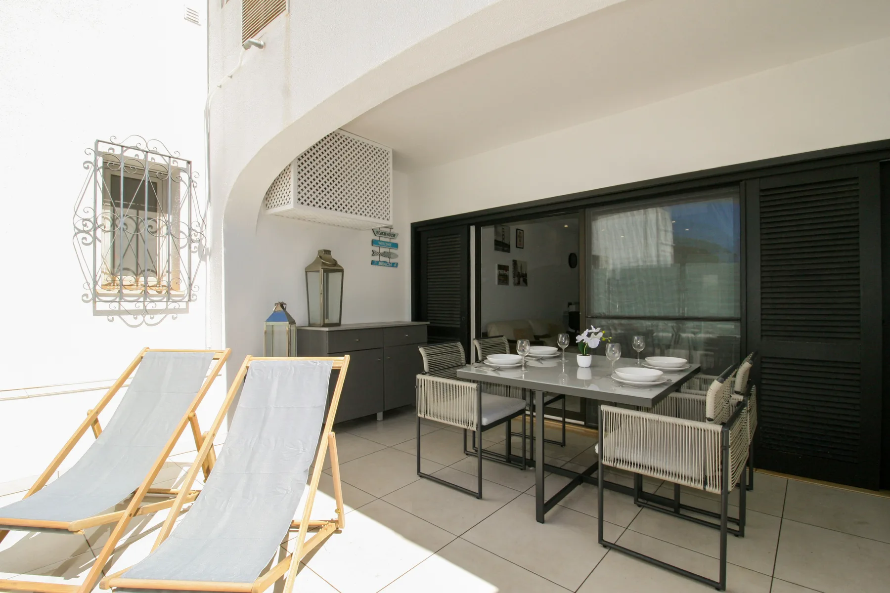 Una terraza amueblada con asientos y una mesa de comedor junto a puertas correderas oscuras.