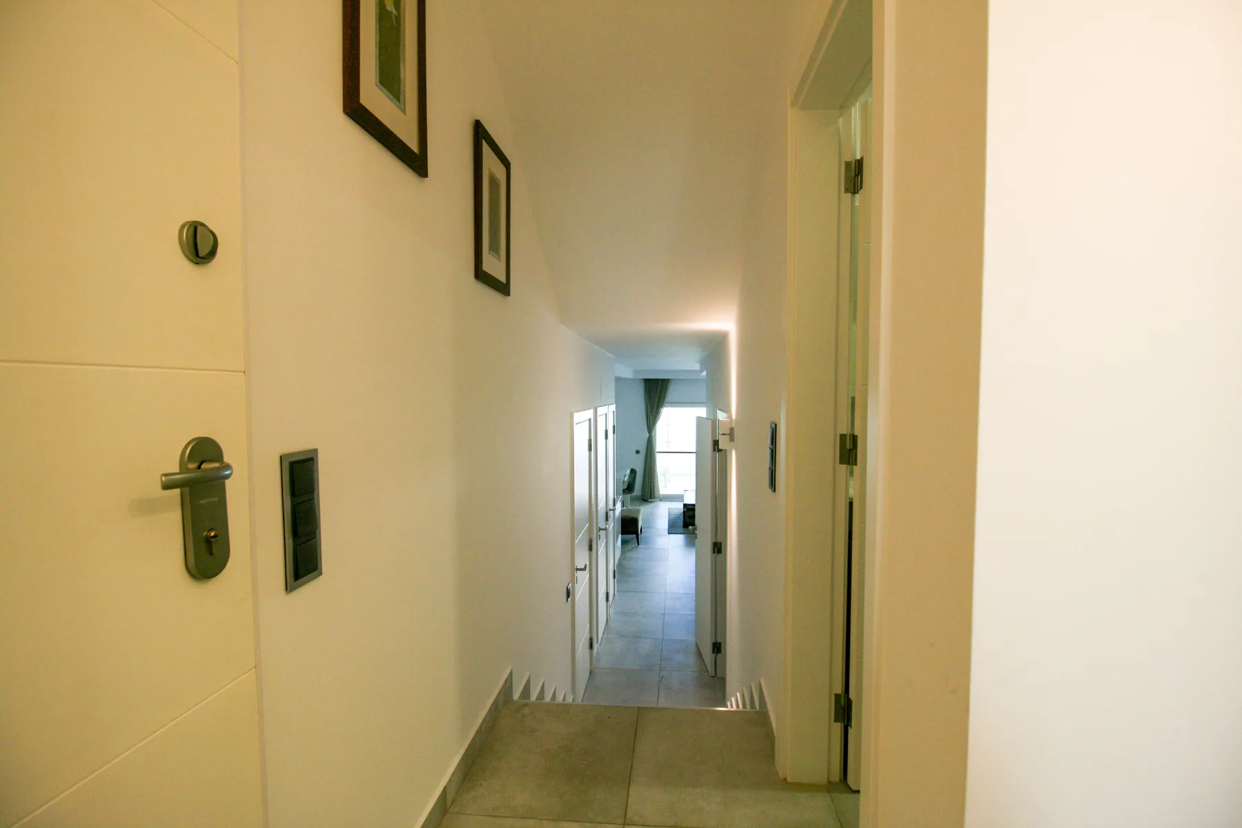 Un pasillo interior estrecho con cuadros enmarcados y una puerta al fondo.