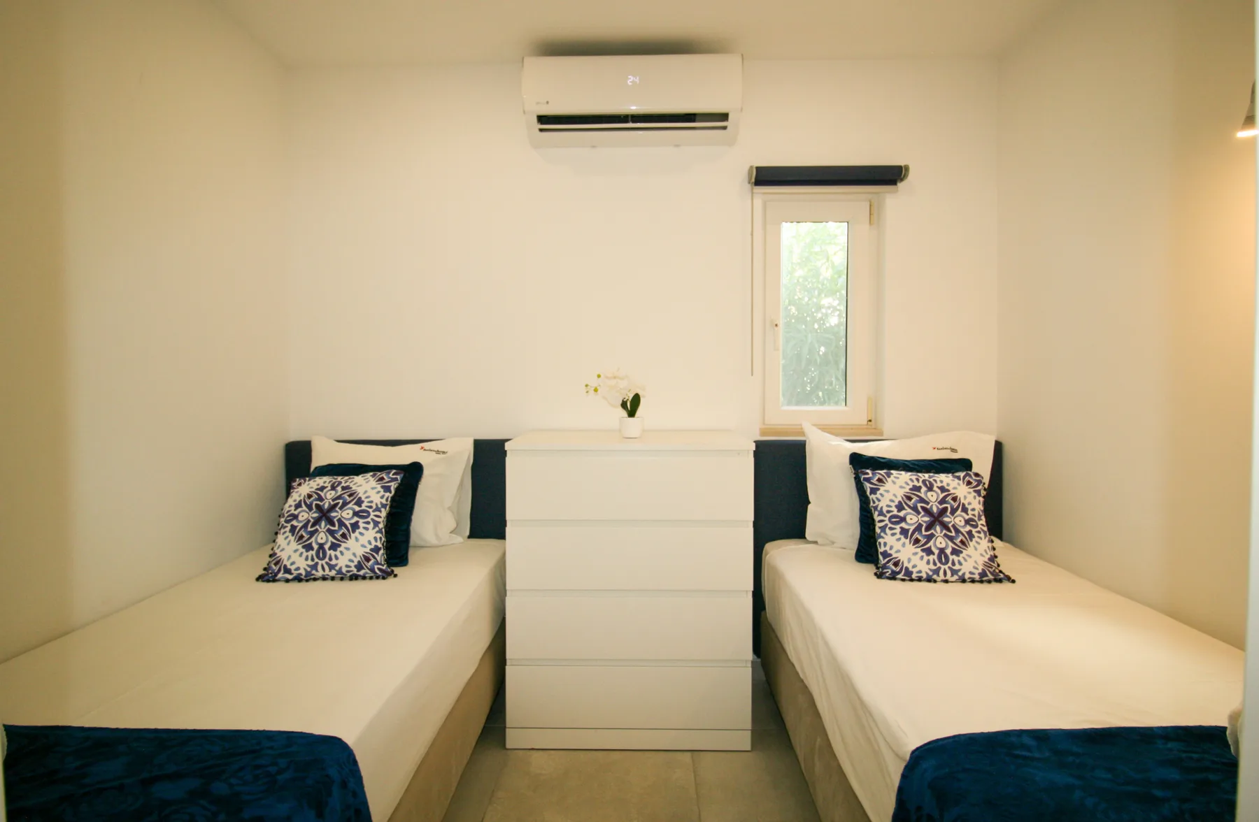 Un dormitorio con dos camas y una cómoda blanca debajo de una ventana.