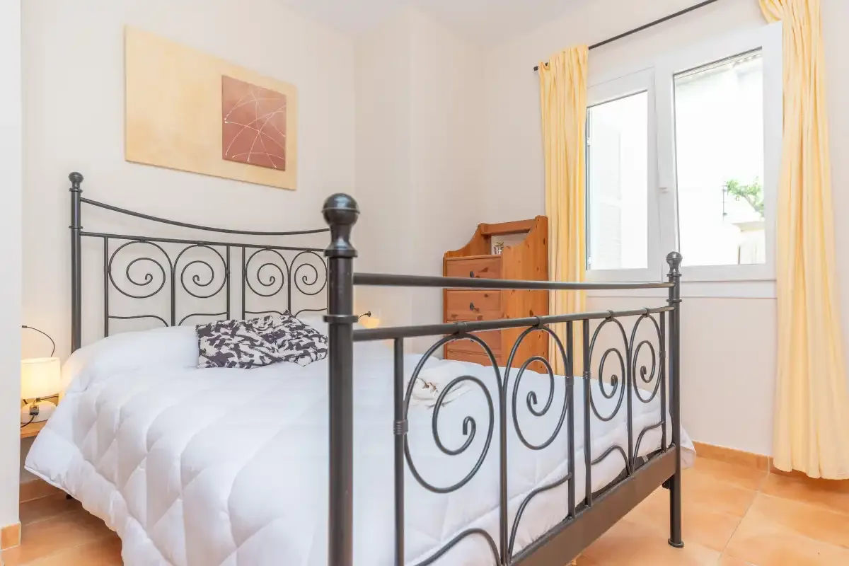 A bedroom with a bed, a metal headboard, and a bright window.