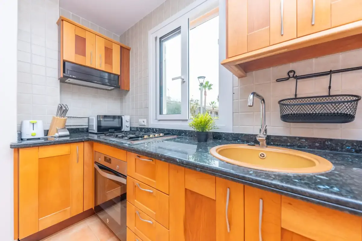 A kitchen with orange cabinetry, dark countertops, and a window.