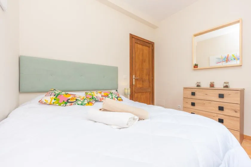 A bedroom with a neatly made bed and a wooden dresser.