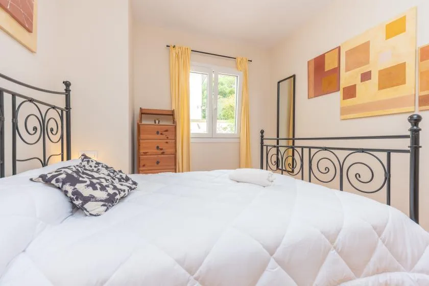 A bedroom with a white bed, black metal headboard, and yellow curtains.