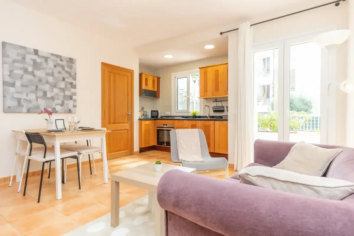 A bright living and dining area opens onto a kitchen, with large windows.