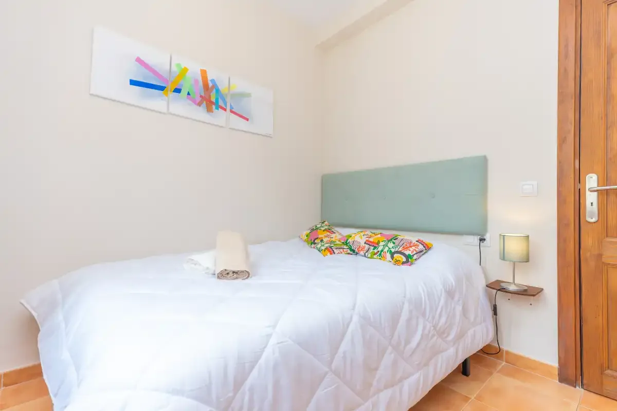 A bedroom with white bedding, colorful cushions, and abstract wall art.
