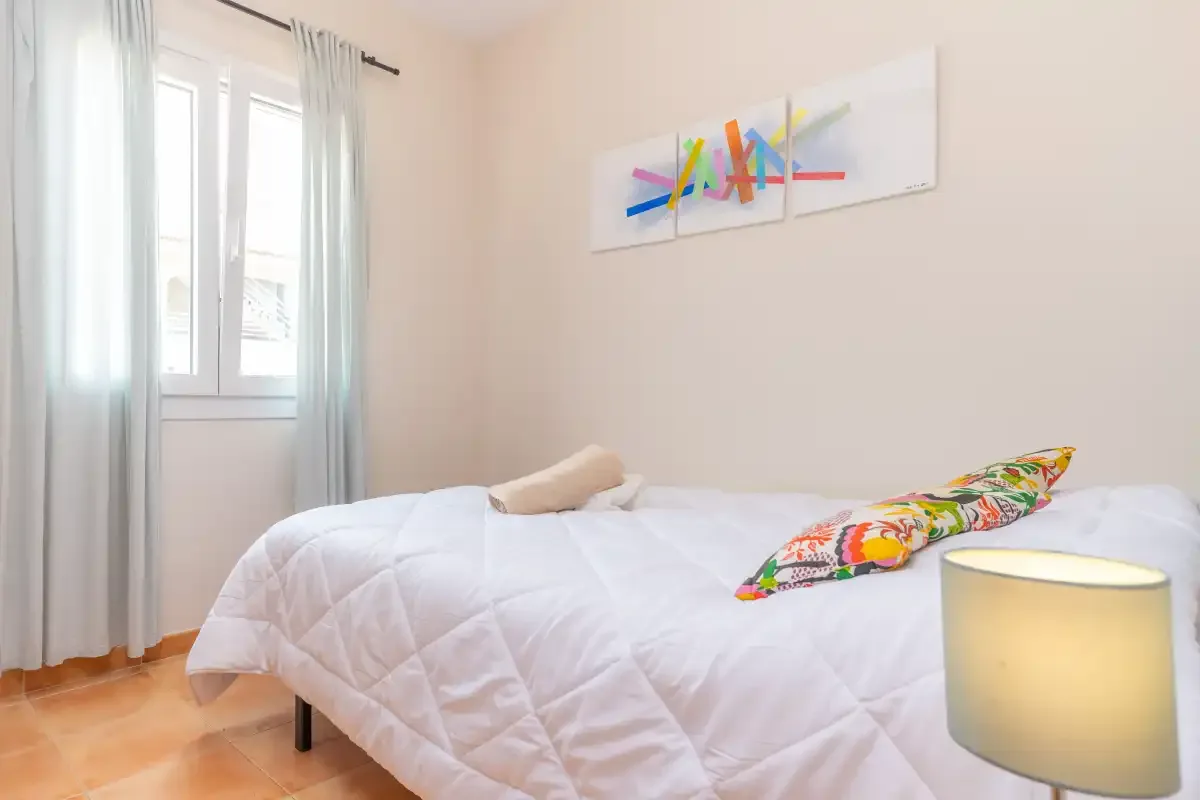 A bedroom with a white bed, colorful pillows, and abstract wall art.