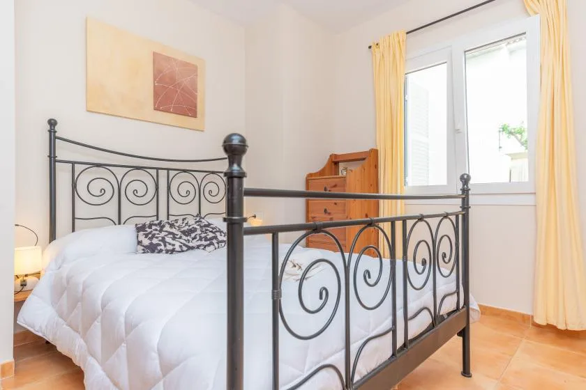 A bedroom with a bed, dark metal frame, and a bright window with yellow curtains.
