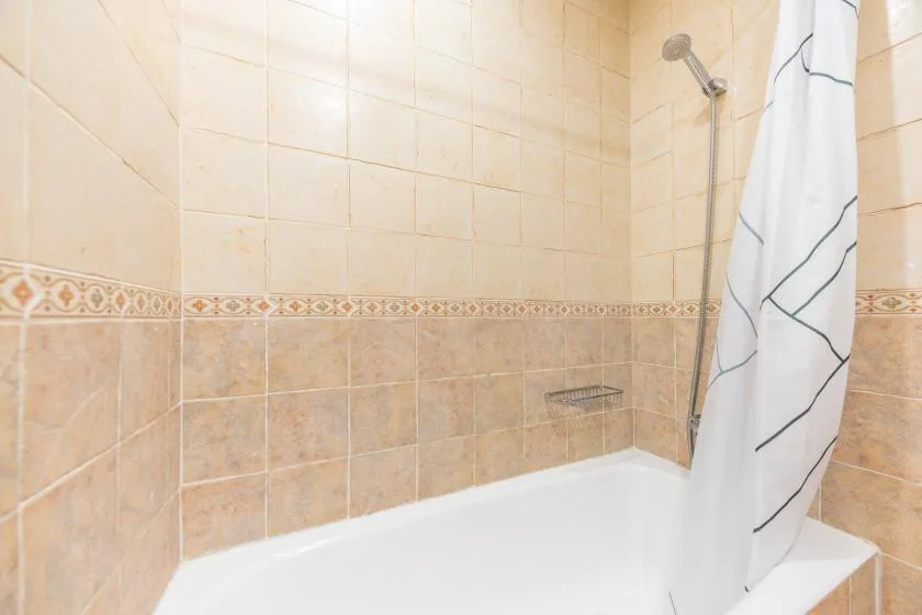 A tiled bathroom with a bathtub, showerhead, and white curtain.