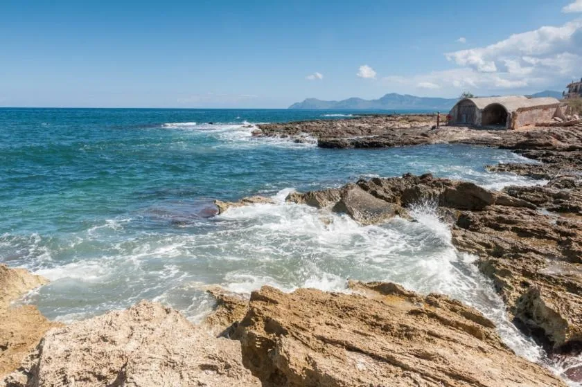 A rocky shoreline with waves breaking beneath a clear blue sky.
