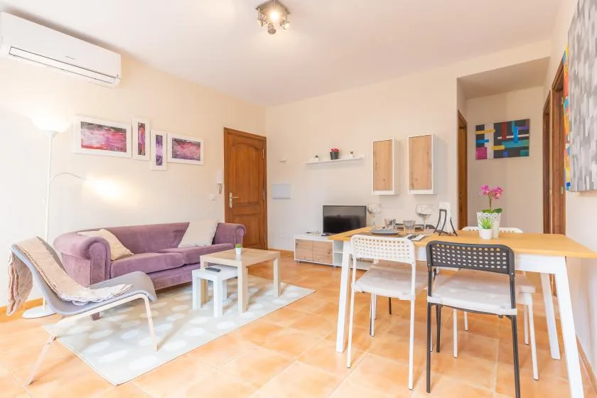 A bright living and dining area with a purple sofa, table, and chairs.
