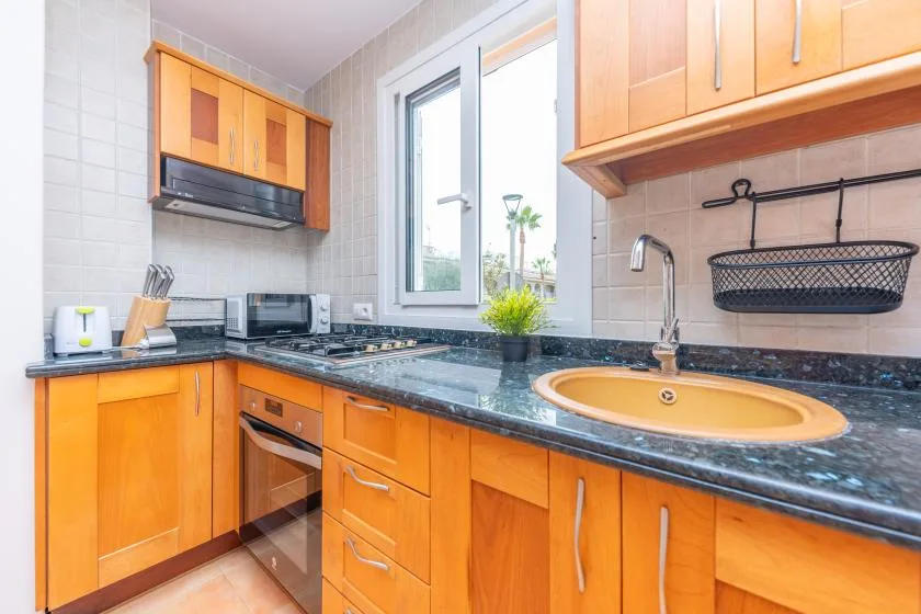 A bright kitchen with wooden cabinets, dark countertops, and a sink beneath the window.
