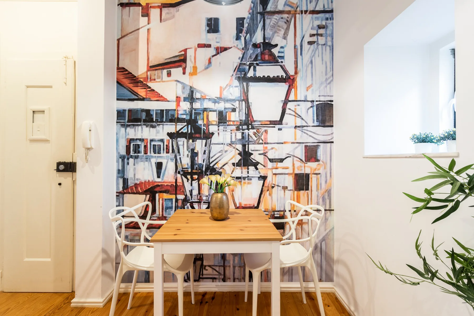 Comedor con una mesa de madera y asientos blancos frente a un mural colorido.