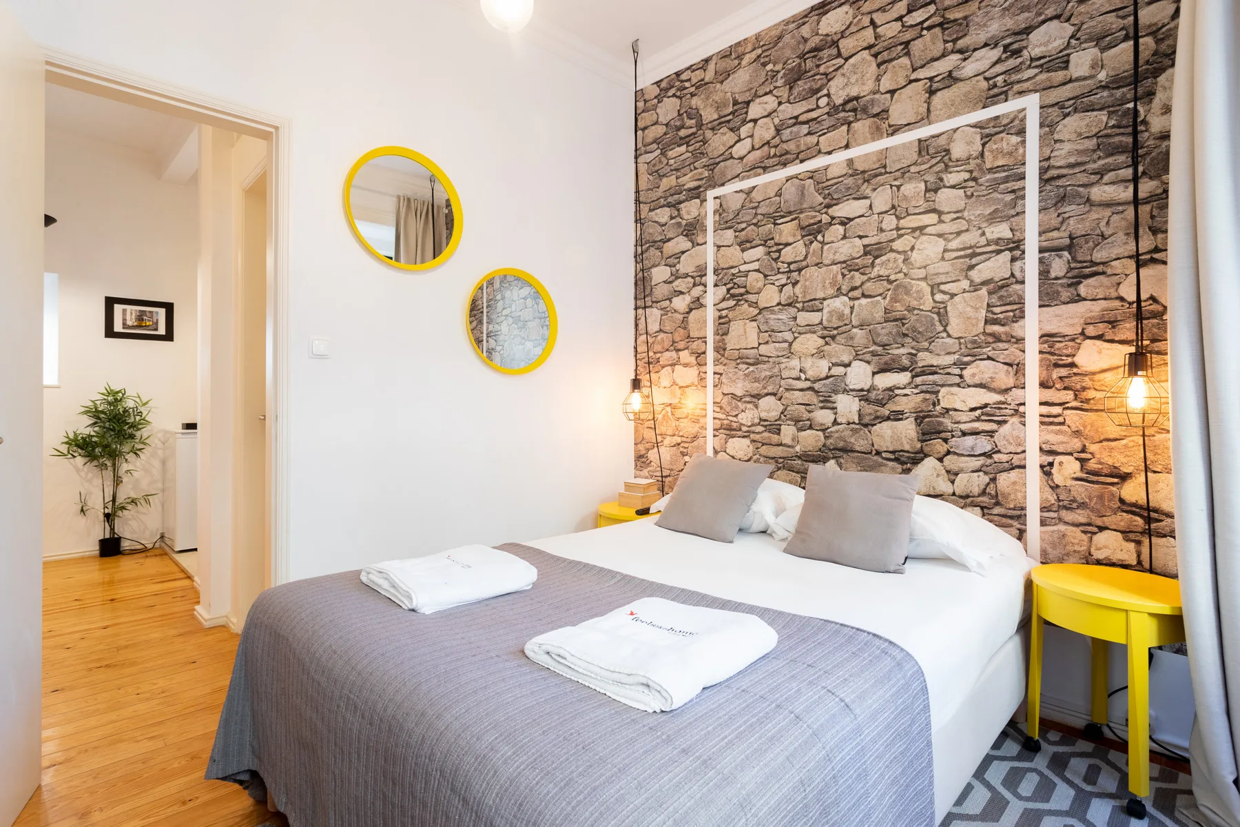 A bedroom with a neatly made bed and a stone-patterned wall.
