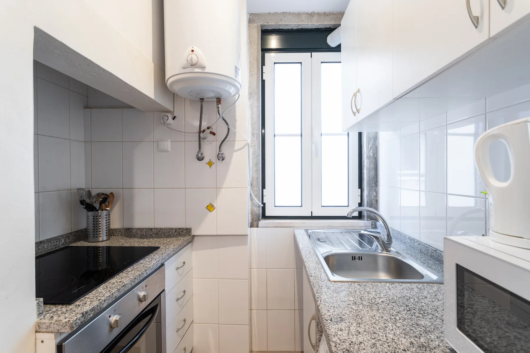 A narrow kitchen with a cooktop, sink, and window.