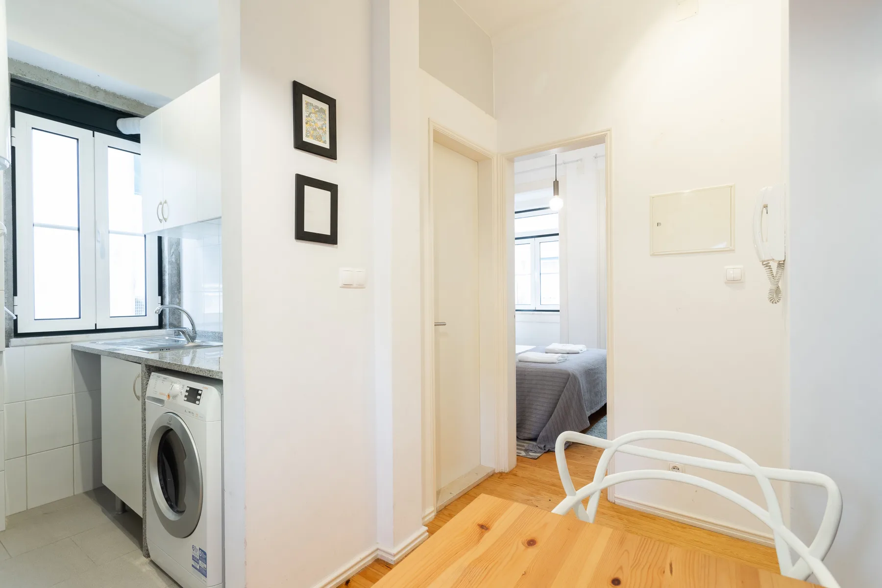 Interior luminoso de un apartamento con una pequeña cocina y un dormitorio visible desde la puerta.