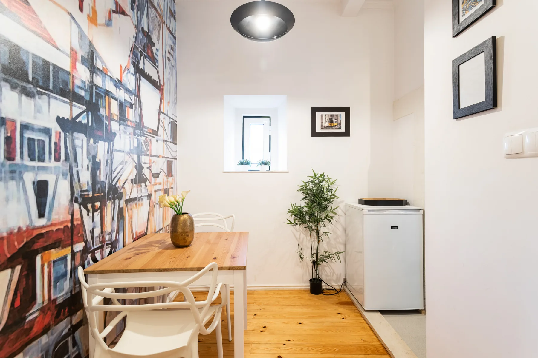 A dining area with a wooden table, white chairs, and a large wall mural.