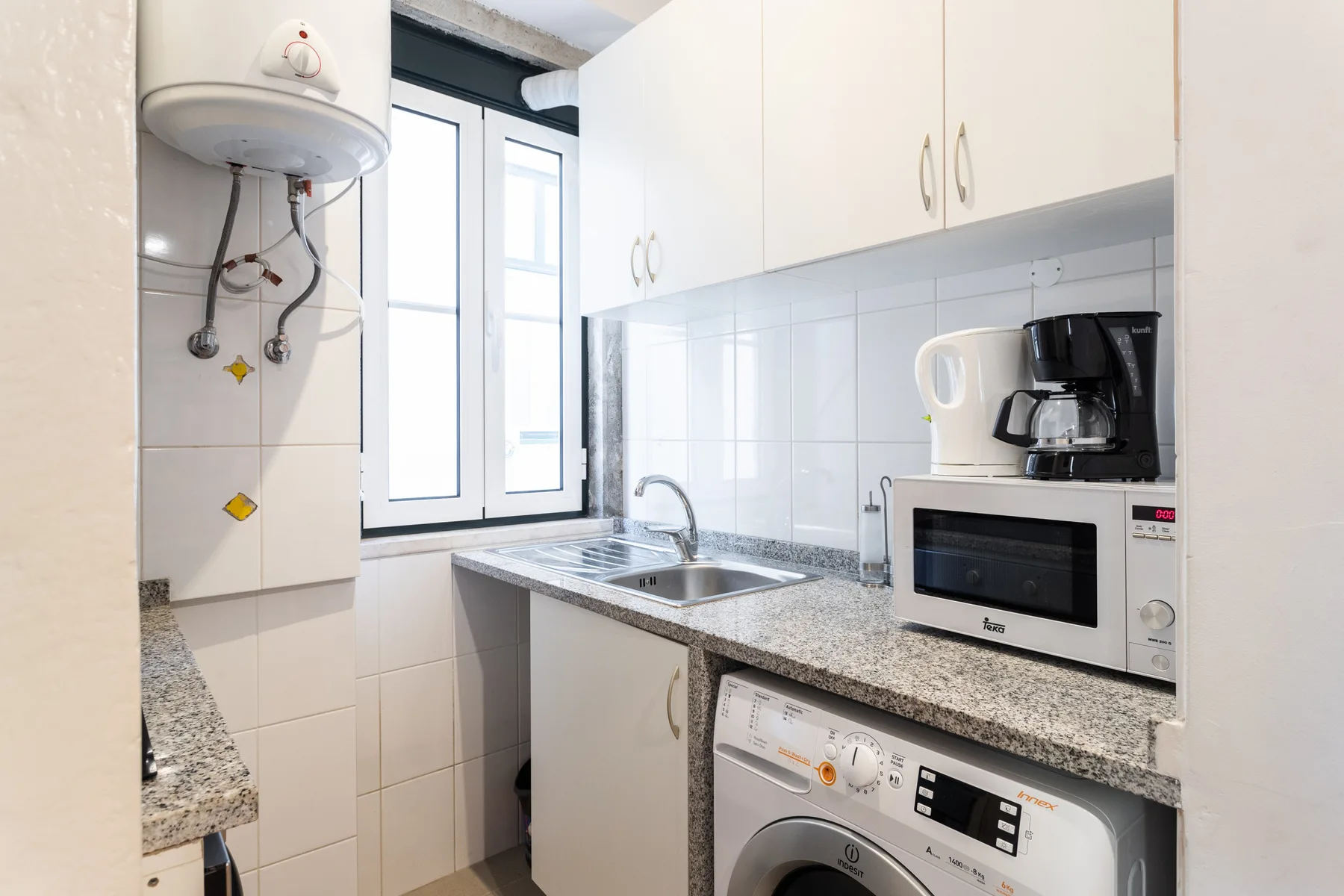 Una cocina compacta con fregadero, electrodomésticos sobre la encimera y lavadora.