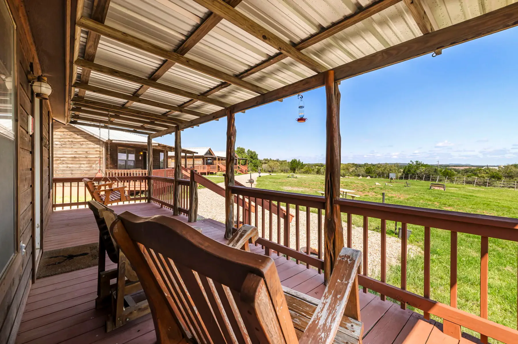 A covered wooden porch has bench seating overlooking a grassy landscape.