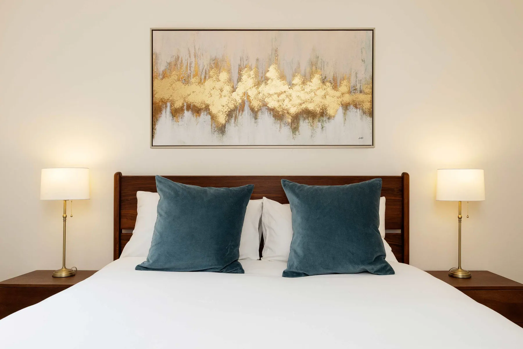 Una cama bien hecha con cojines azul verdoso está bajo una pintura abstracta.