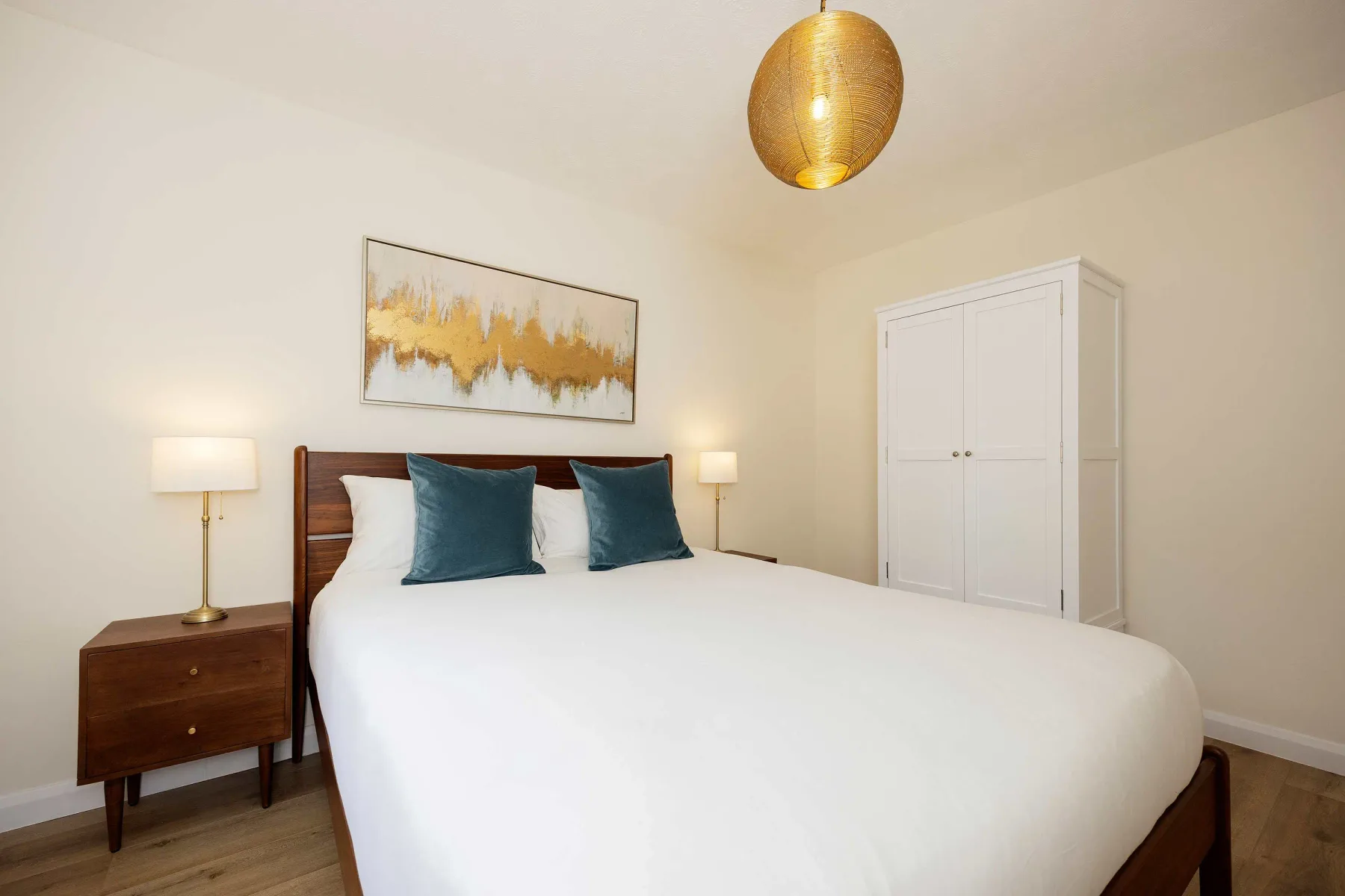 Un dormitorio con una cama bien tendida, mesitas de noche y un armario blanco.
