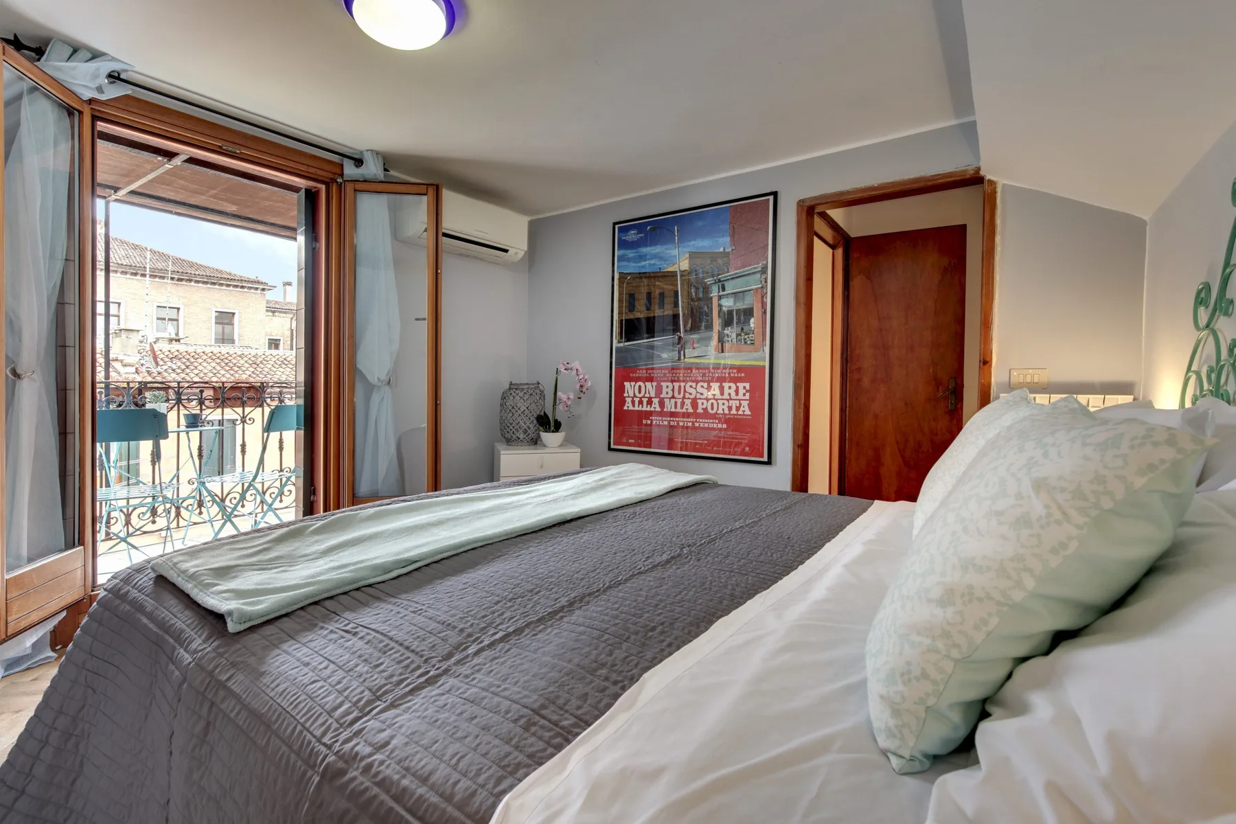 Un dormitorio con una cama junto a una ventana abierta y un balcón.