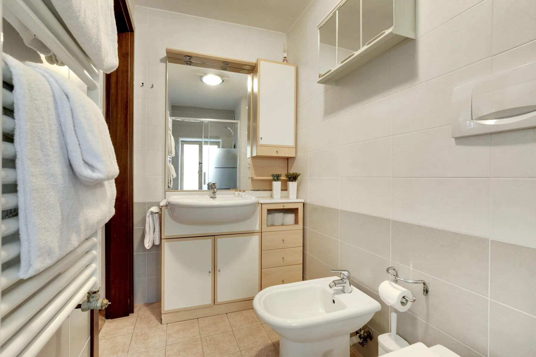 Un baño con azulejos, lavabo, espejo y toallero calefactable.