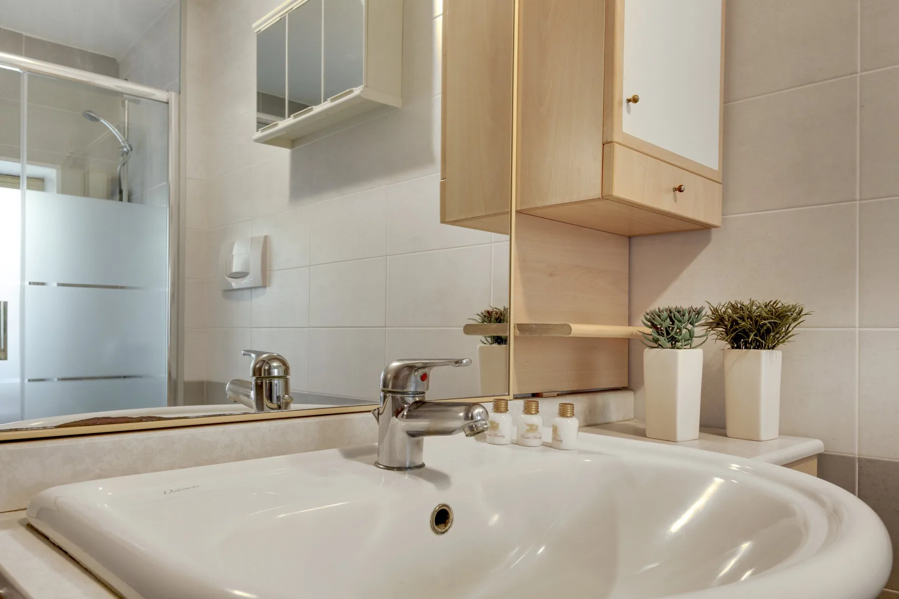 Un lavabo de baño con azulejos, espejo y pequeñas plantas en macetas.