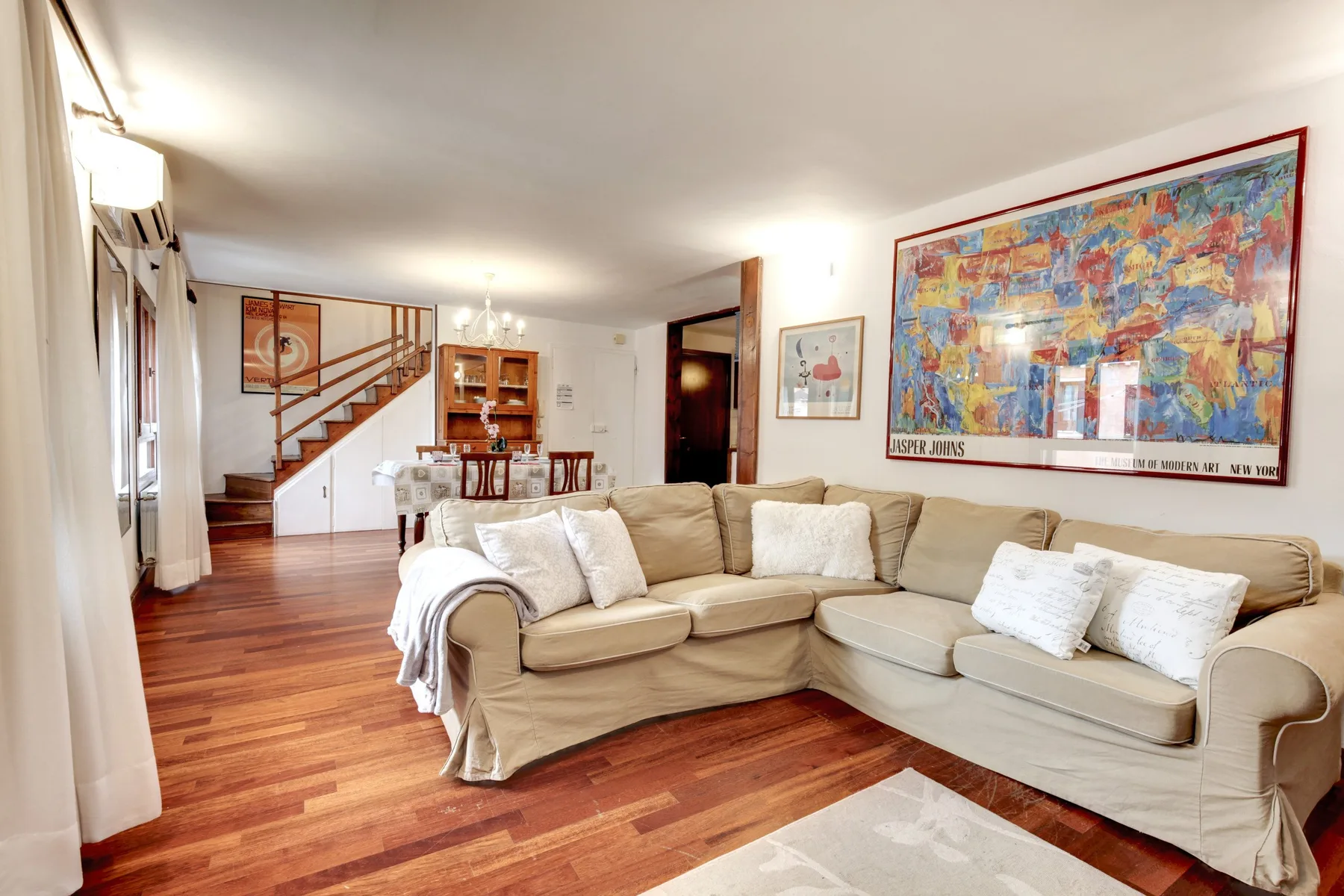 Una sala de estar con un sofá seccional beige y una obra colorida en la pared.