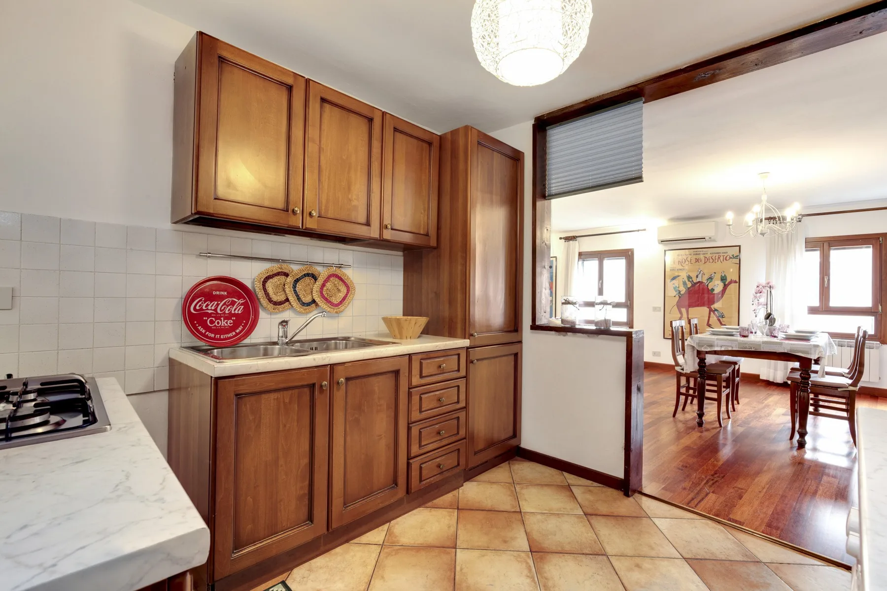 Una cocina con gabinetes de madera se abre a un comedor con mesa y sillas.