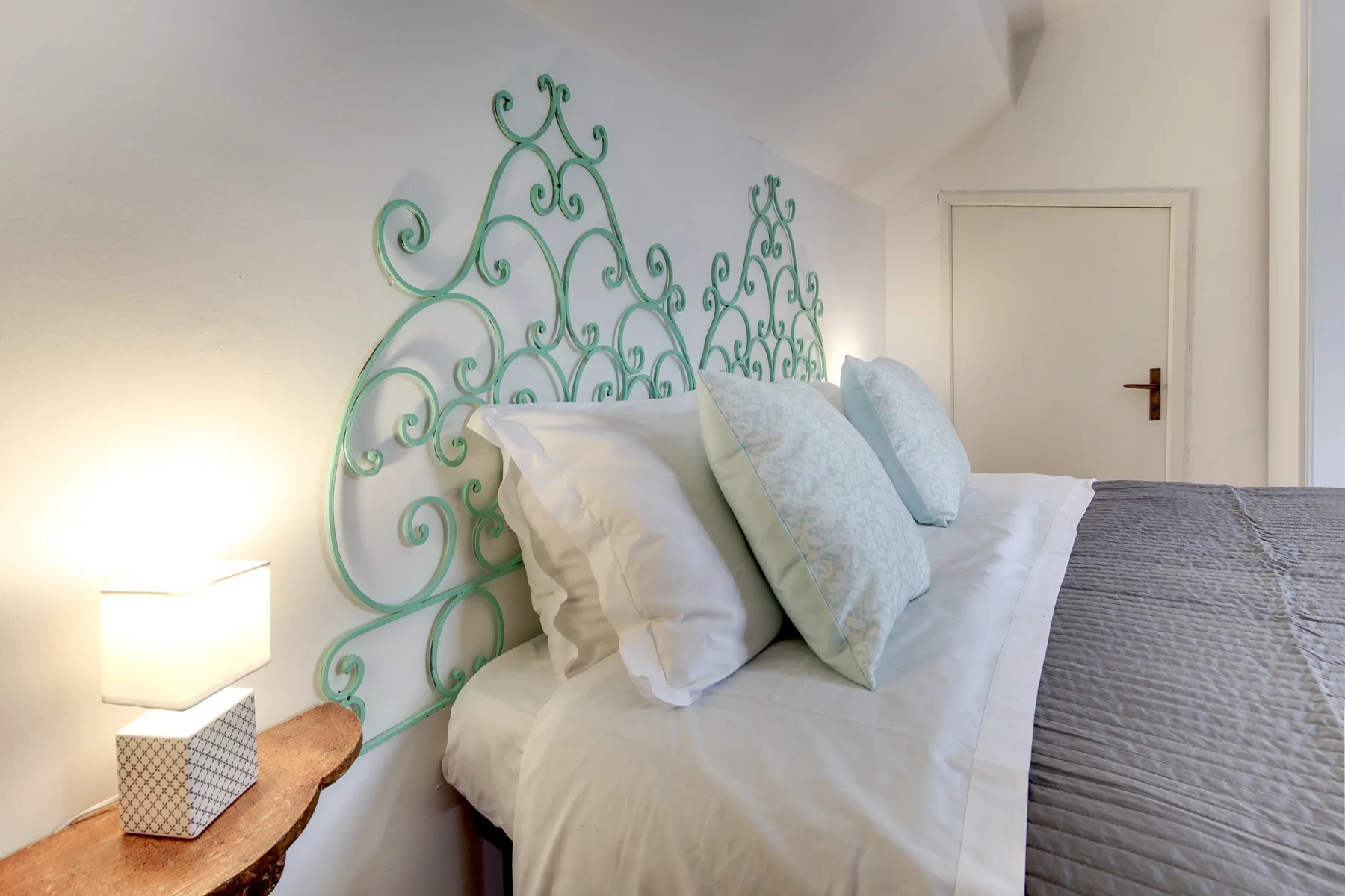 Un dormitorio con ropa de cama blanca, cabeceros verdes decorativos y una lámpara de noche.