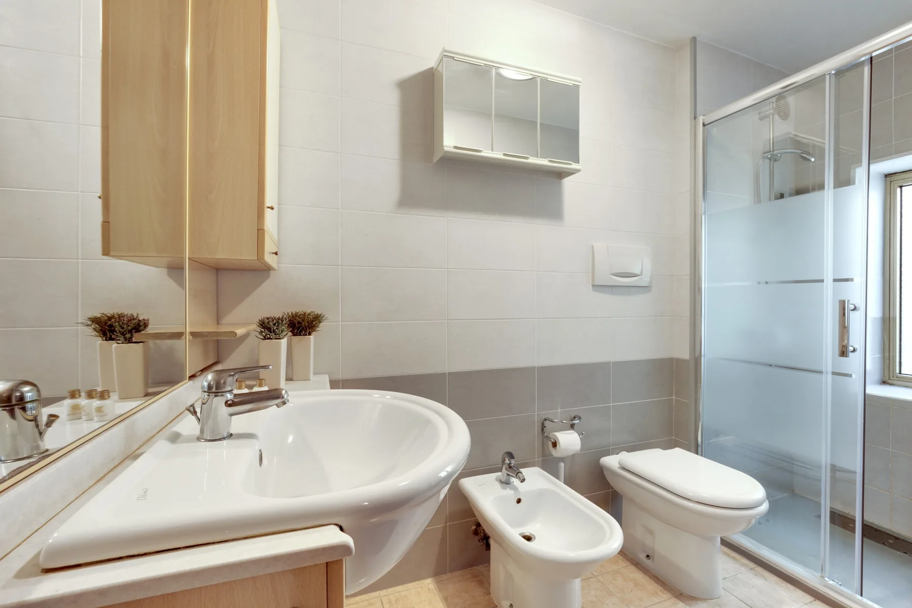 Un baño alicatado con lavabo, inodoro, bidé y ducha de cristal.