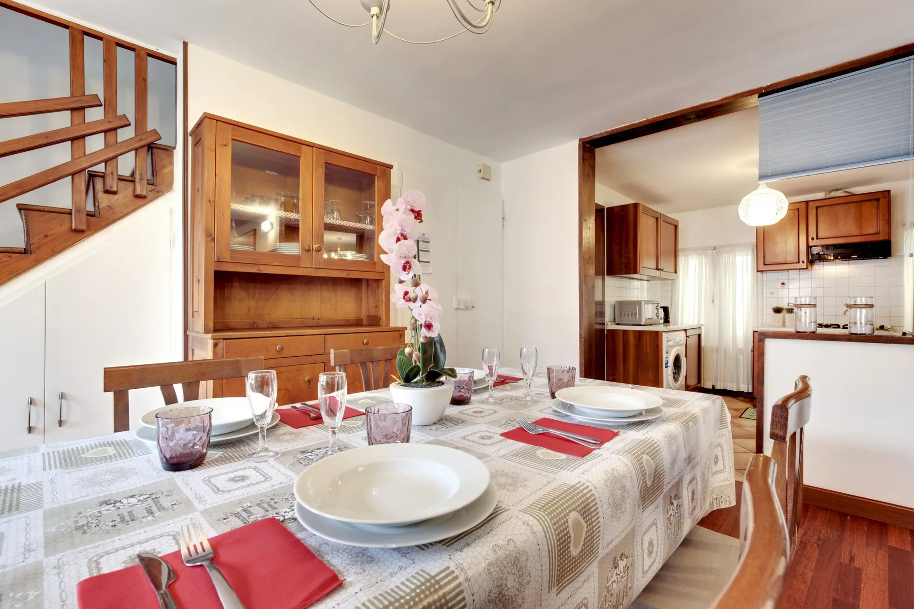 Un comedor con la mesa puesta junto a una escalera de madera y una cocina.